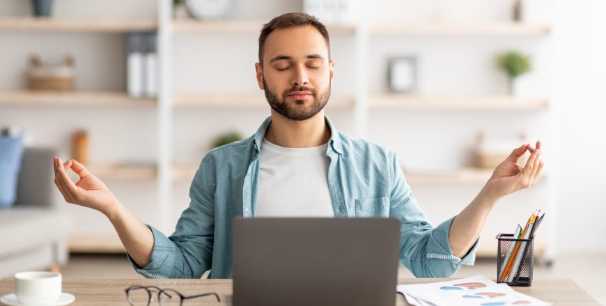 Workplace stress management. Calm Caucasian man meditating with closed eyes in front of laptop pc at home office